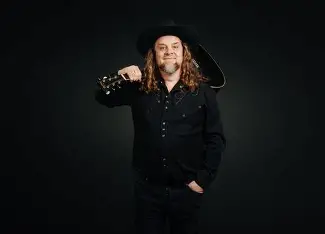 Johnny Trash op het podium met gitaar en cowboyhoed tijdens een comedy- en muziekoptreden.